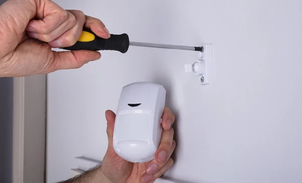 Hand using a screwdriver to install an advanced sensor device on a white wall, highlighting advanced sensor installation services in Palm Beach Gardens, FL.