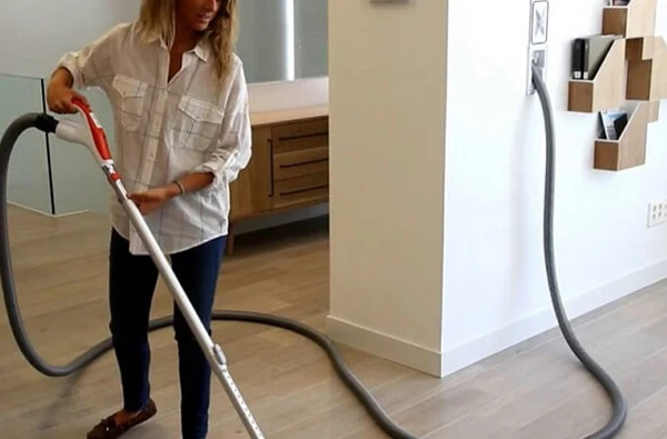 Person vacuuming with central vacuum system hose in a modern home, promoting efficient central vacuum system installation services in Palm Beach Gardens, FL.