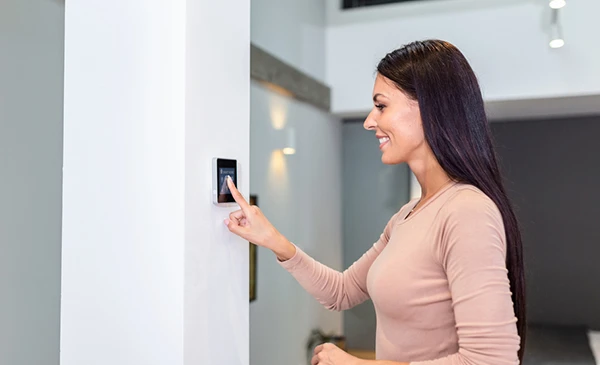 Woman using a wall-mounted smart home automation control panel for innovative home automation installation services in Palm Beach Gardens, FL.
