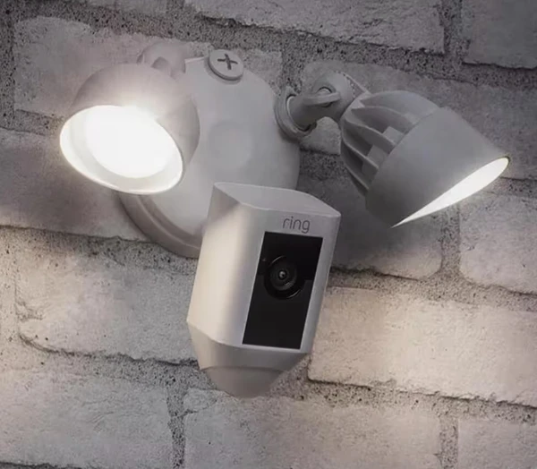 Outdoor security floodlight with built-in surveillance camera mounted on a white brick wall, showcasing home security and intercom system installation in Palm Beach Gardens, FL.