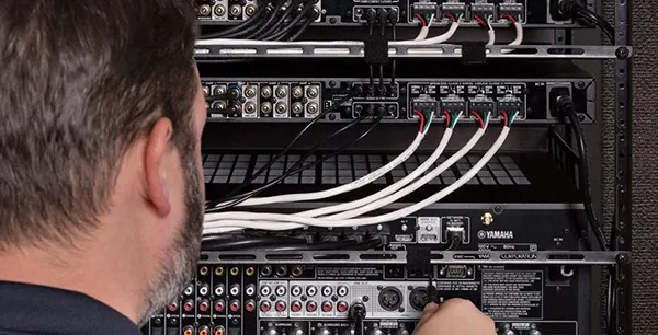 Close-up of technician’s back wiring a multi-room audio system rack with networking cables in Palm Beach Gardens, FL.